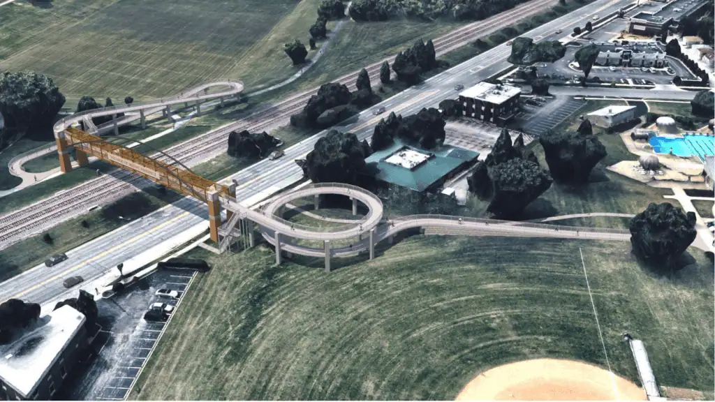 A rendering shows an aerial view of a circular ramp leading up to a pedestrian bridge across a four-lane road and three railroad tracks.